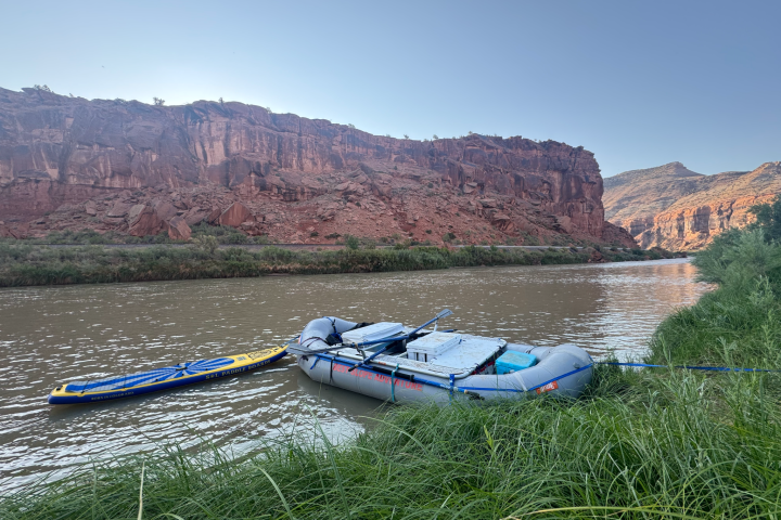 Inflatable raft and paddleboard on a river by red cliffs under clear sky.