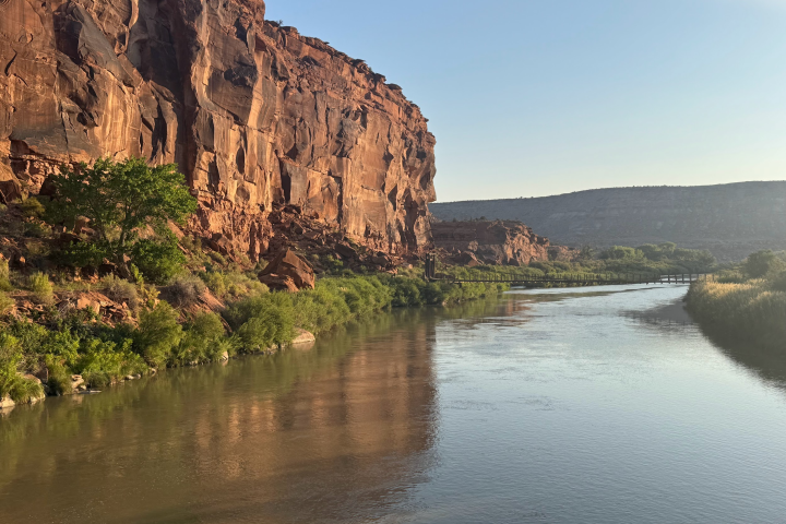 River flowing alongside red rock cliffs under a clear blue sky.